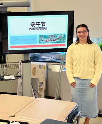  A woman stands in front of a screen displaying Chinese text and an image of a dragon boat.